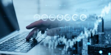 Close up of hand using laptop with creative candlestick forex chart or graph on blurry wide city background. Financial trade market and stock concept. Double exposure.