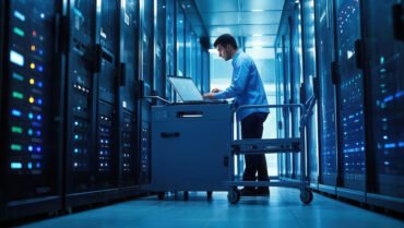 Young businessman working with laptop in server room data center. Toned image.